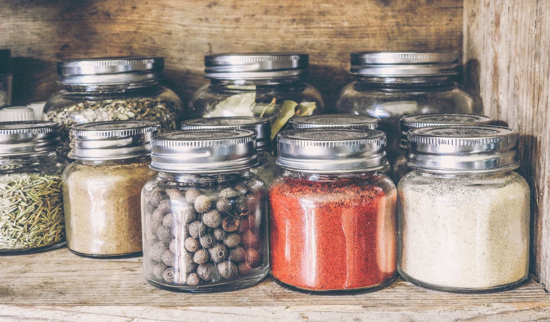 Colourful array of spices and dried herbs in jars on pantry shelf