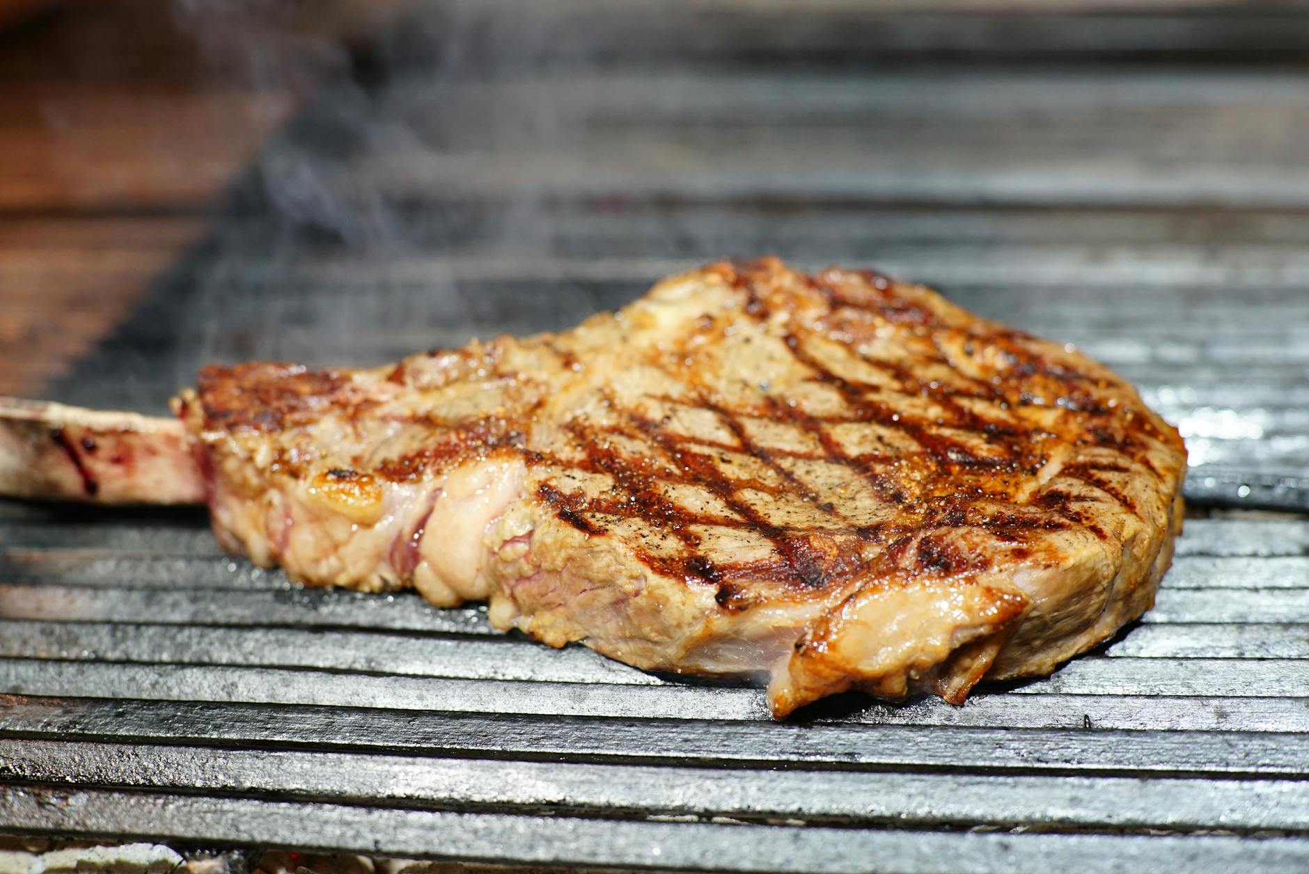 Thick beef ribeye steaks sizzling on a barbecue grill outdoors